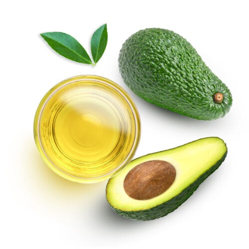 Avocado oil in glass bowl and fresh avocado fruit with green leaf isolated on white background. Top view. Flat lay.