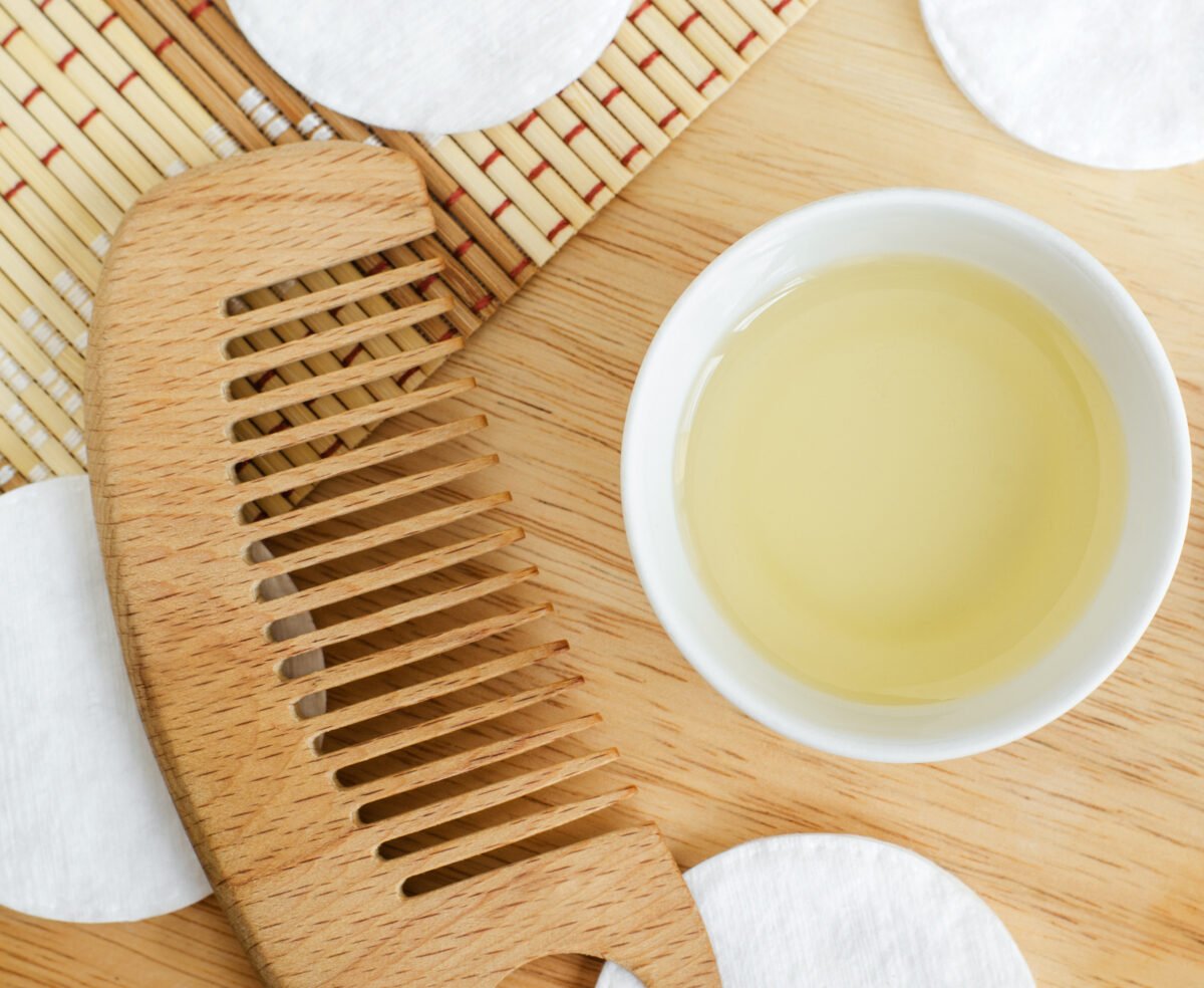 castor oil, cotton pads and wooden hairbrush. Ingredients for preparing homemade hair mask. Natural beauty treatment recipe and zero waste concept. Top view, copy space.