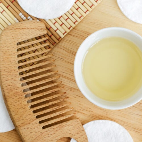 castor oil, cotton pads and wooden hairbrush. Ingredients for preparing homemade hair mask. Natural beauty treatment recipe and zero waste concept. Top view, copy space.