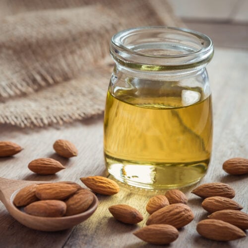 Almond oil in glass bottle and almonds on wooden table