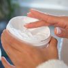 Woman dipping finger into jar of moisturizing cream for her face, body care and wellness