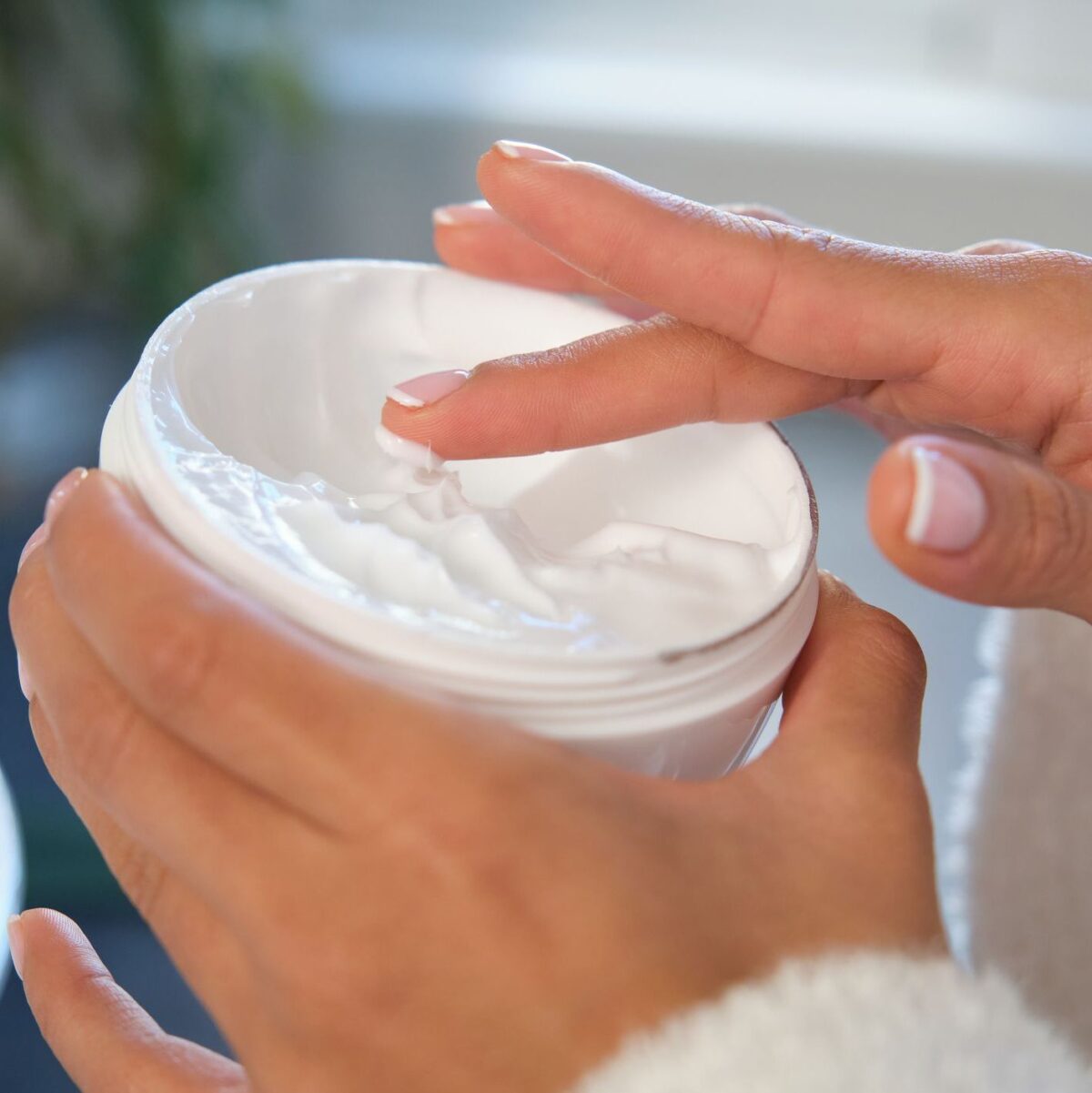 Woman dipping finger into jar of moisturizing cream for her face, body care and wellness