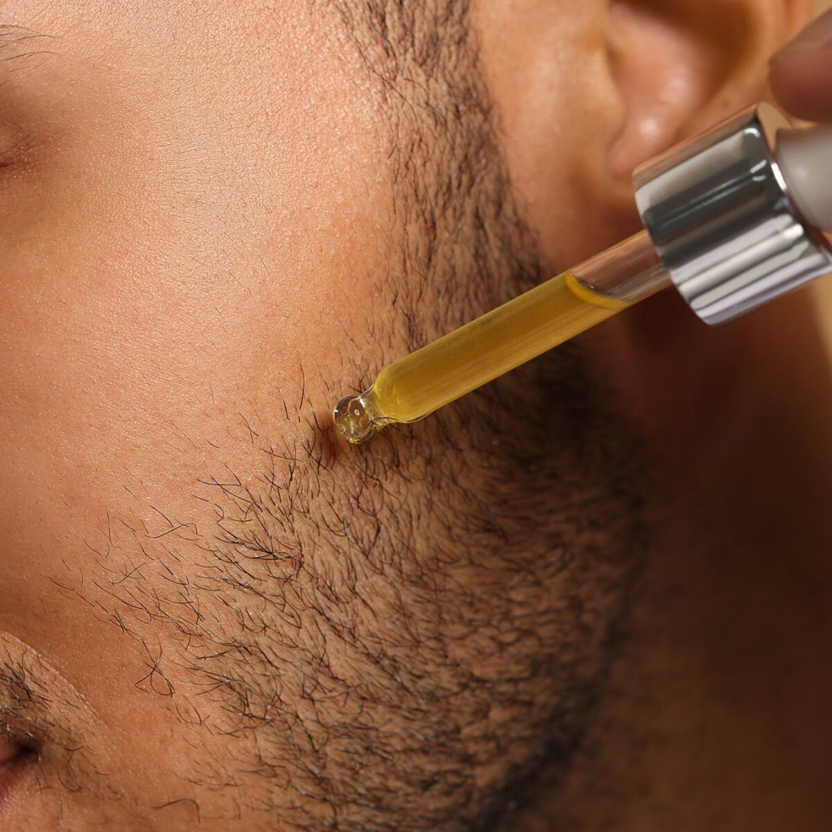Handsome man applying cosmetic serum onto face, closeup